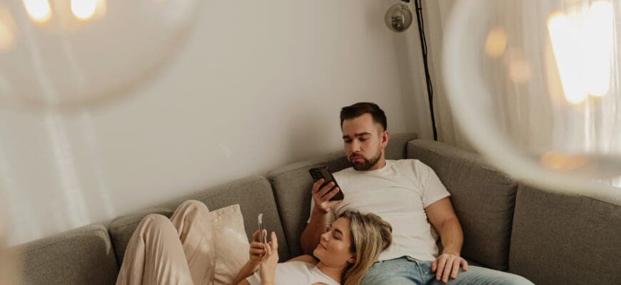 A man and a woman sitting on a living room couch and looking at their phones